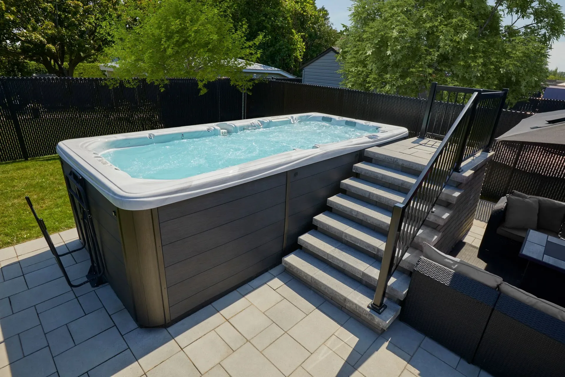 Dynasty swim spa set into a paver patio, its full length in frame beside the deck steps